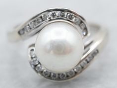 "What an elegant combination of colors! We love the way this vintage cocktail ring evokes the past, like a 1920's dress that flows with cream satin and sparks with sequins. This is a lovely pearl, a velvety gem with a sophisticated color! The setting is white gold, a swirling take on the classic bypass style, studded with diamond accents! Metal: 14K White Gold Gem: Pearl Gem Measurements: 8.0 mm, Round Accents: 22 Diamonds totaling .22 Carats, H in Color, SI1 in Clarity Ring Size: 5.75 Marks: \" White Gold Pearl Ring, 1920's Dress, Pearl Anniversary, Petite Earrings, Ring Pearl, Gold Pearl Ring, Vintage Cocktail Ring, Pearl And Diamond Ring, Bypass Ring