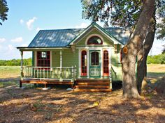 a small green house sitting in the middle of a field next to a large tree