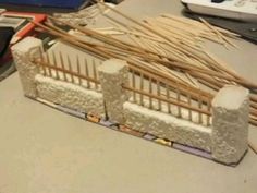 a model of a fence made out of bricks and bamboo sticks is on the table