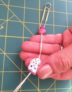 a hand holding a small pink and white bead on a string with a pin in it