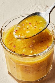 a spoon full of liquid sitting in a glass jar on top of a white surface