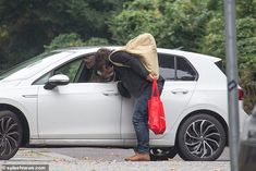 a man leaning on the door of a white car with a red bag in his hand