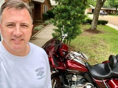 a man standing next to a red motorcycle in front of a house on the street