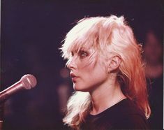 a woman with blonde hair standing in front of a microphone and looking off into the distance