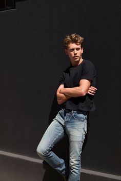 a young man leaning against a wall with his arms crossed