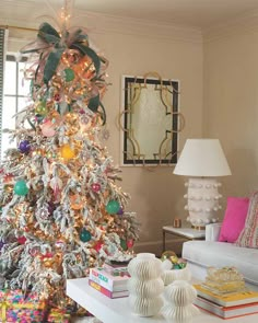 a decorated christmas tree in the corner of a living room with white furniture and colorful decorations