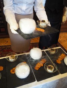 a person in white gloves is serving food to others on black trays and plates