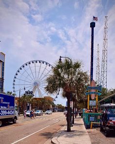 an amusement park with ferris wheel and cars parked on the side of the road in front of it