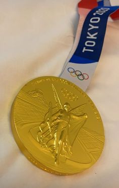 a gold medal with a ribbon around it on top of a white sheet that says tokyo olympics