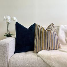 two striped pillows on a white couch next to a vase with three flowers in it