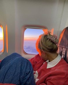 a woman sitting on an airplane seat looking out the window at the sunset and clouds