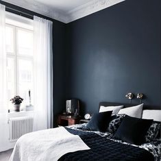 a bedroom with dark blue walls and white bedding, black comforter and pillows