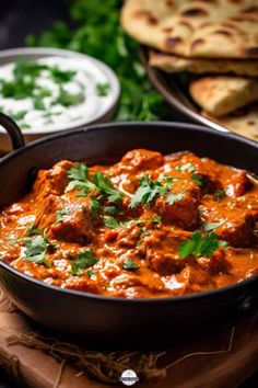 a pan filled with meat and sauce on top of a wooden cutting board next to pita bread