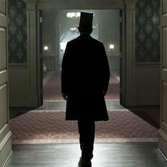 a man in a suit and top hat walking down a hallway with an open door