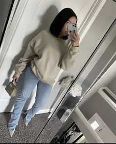 a woman taking a selfie in front of a mirror wearing jeans and a sweater