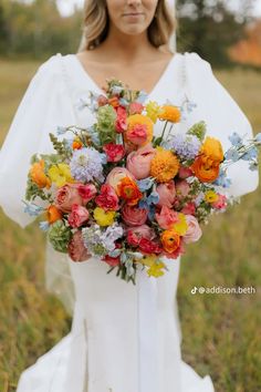 a woman in a white dress holding a colorful bouquet with orange, yellow and pink flowers