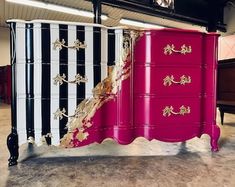 a pink and black dresser with gold decorations on it's sides in an empty room