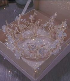 a tiara in a pink box on a wooden table with sparkles around it