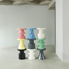 four different colored vases sitting next to each other on a cement floor in front of a white wall