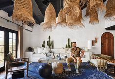 a man sitting on a couch in a living room with lots of wicker hanging from the ceiling