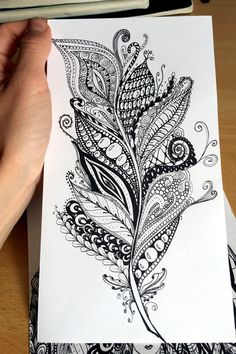 a hand holding a piece of paper with an intricate design on it and a pen next to it