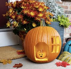 a pumpkin carved to look like a house with a face in the center and flowers behind it