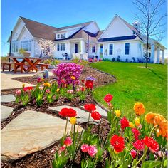 colorful flowers are blooming in front of a white house with picnic tables on the lawn