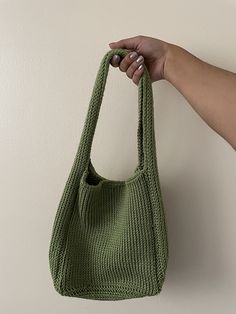 a hand holding a green knitted bag on a white wall with the handle up