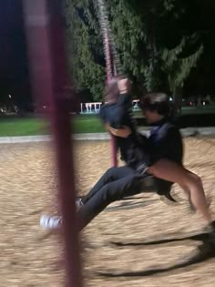 a man and woman are playing on a swing set at the park in the evening