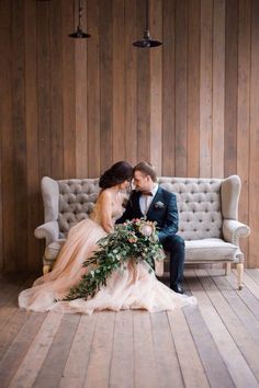 a bride and groom sitting on a couch in front of wooden paneled walls, dressed in tuxedo