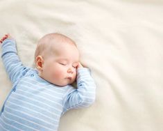 a baby laying on top of a bed with his head resting on his hands and eyes closed