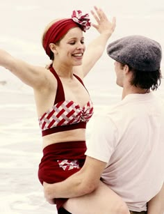 a woman in a bathing suit standing next to a man on the beach with her arms up