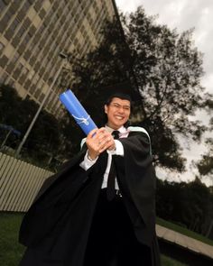 a man in graduation robes holding a blue bat