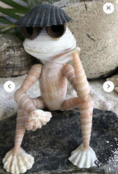 a small toy frog sitting on top of a rock next to some rocks and sea shells