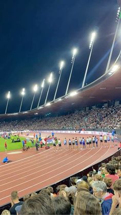 a group of people standing on top of a track in front of a stadium filled with spectators