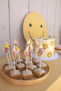 there are cupcakes with faces on them sitting in front of a yellow cake