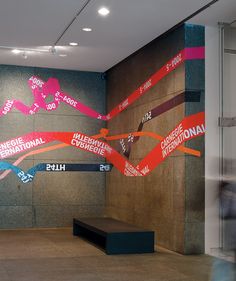 a large wall with many different colored ribbons on it and people walking by in the background