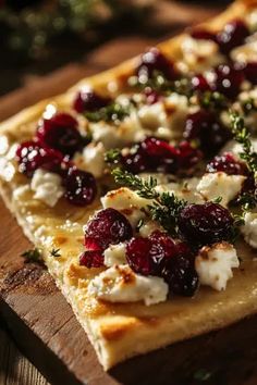 a flatbread with cheese, cranberries and herbs is on a cutting board