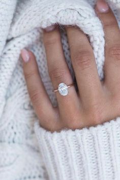 a woman's hand with a diamond ring on her finger, wrapped in a white sweater