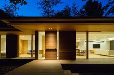 a modern house with large sliding glass doors and wood accents at night, lit up by lights on the windows