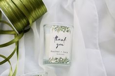 a couple of candles sitting on top of a white cloth next to a spool of green ribbon