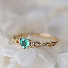 a close up of a ring with a heart shaped blue stone on the side and white flowers in the background