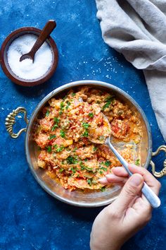 a person holding a spoon in a bowl filled with food