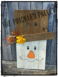 a wooden block with a face painted on it and flowers in front of a fence