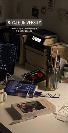 a desk with a laptop, books and other items on it in front of a computer monitor