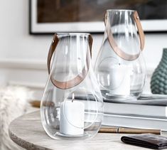 two clear vases sitting on top of a wooden table next to a white candle