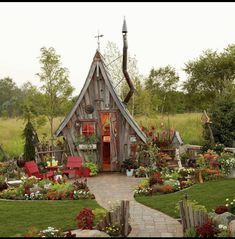 a house made out of wooden planks in a garden with lots of flowers and trees