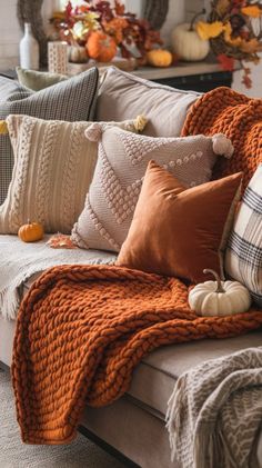 a couch covered in pillows and blankets with fall decorations on the back wall behind it