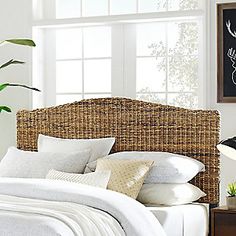 a wicker headboard with white linens and pillows on a bed in a bedroom