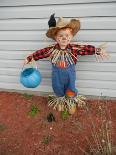 a little boy dressed in scarecrow clothes and a hat holding a blue pot with two black birds on it